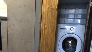 Un lavadero con lavadora, puerta de madera y suelo de baldosas.