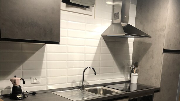 Cocina moderna con pileta de acero inoxidable, encimera negra y muebles grises.