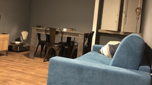 Una habitación con un sofá azul, una mesa de comedor con sillas, una balanza y un armario.