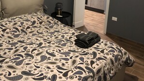 Un dormitorio con cama, mesita de noche, lámpara y puerta que da a un baño.