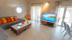 Una sala de estar moderna con un sofá, una mesa de centro, televisor y un amplio ventanal con cortinas.