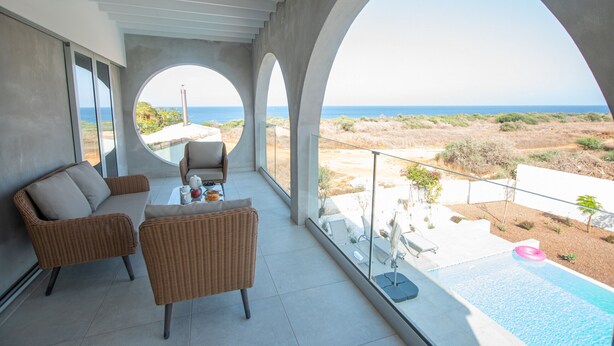 Un balcón con mobiliario de mimbre, una piscina y vista al mar.