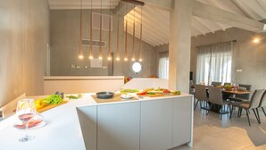 Una cocina moderna con una isla central, iluminación colgante y un comedor con una mesa redonda y sillas.