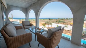 Un balcón con mobiliario de mimbre, una mesa de vidrio y vistas al océano y al paisaje.