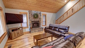 Un salon avec une cheminée en pierre, un canapé en cuir, une table basse en bois et un téléviseur posé sur un meuble.
