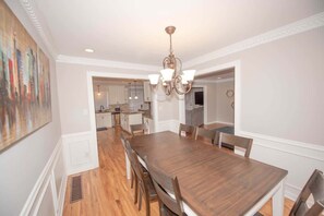 A dining room with a wooden table and chairs, a chandelier, and a view into the kitchen.