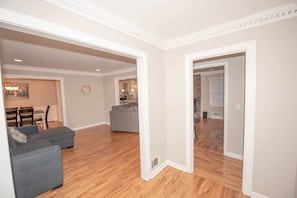 A spacious living area with a grey sofa, wooden flooring, and a kitchen in the background.