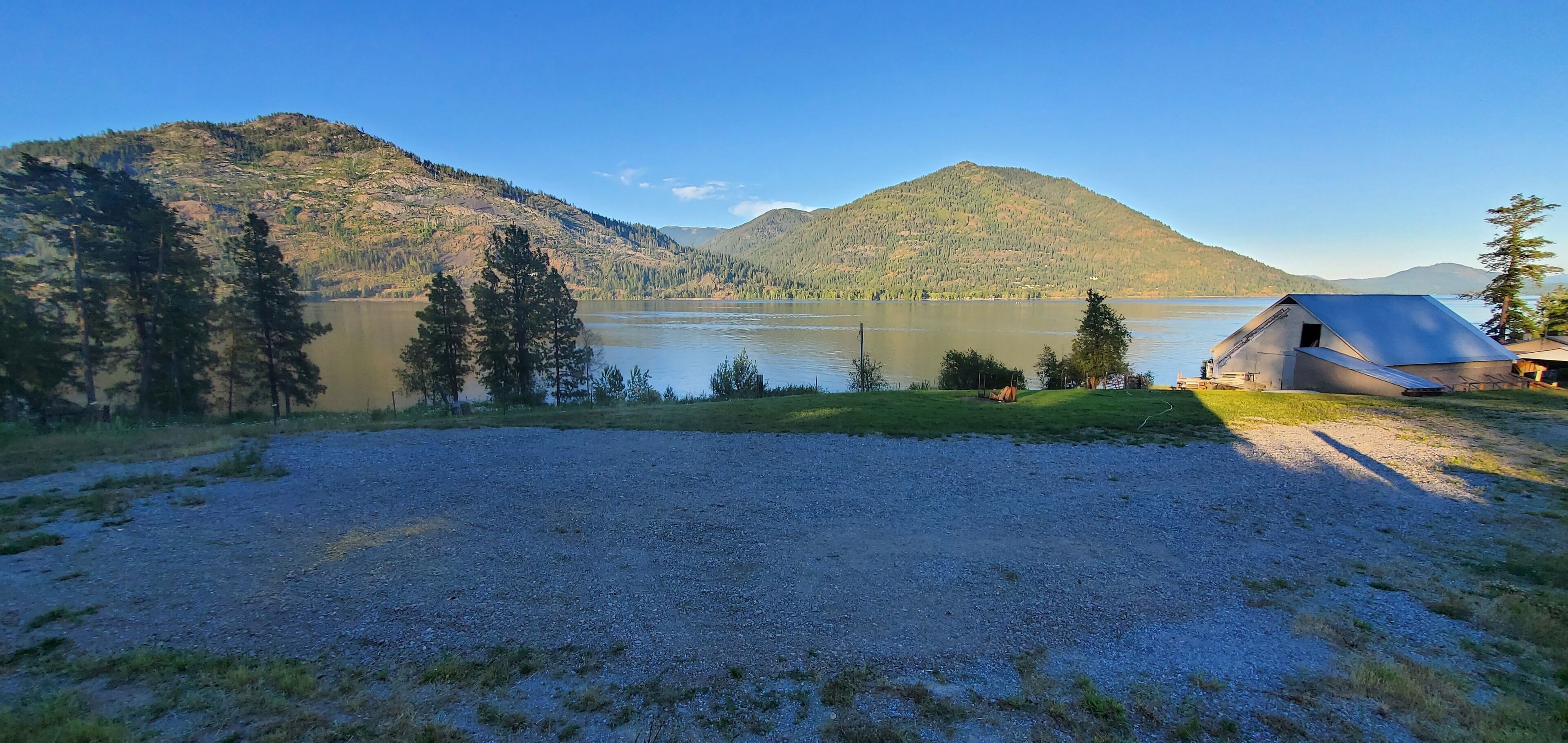A lakeside cabin with a gravel driveway and a small lawn area.