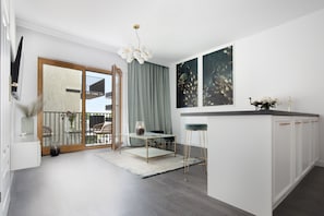 A modern kitchen with a dining area, featuring a glass-top table, bar stools, and a view to the outside.
