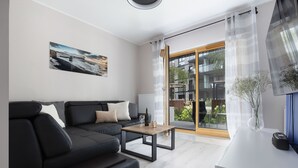A modern living room with a black sofa, a wooden coffee table, and a large window with a view of a building and greenery. - Elite Apartments Nadmotławie Prestige (Gdansk)