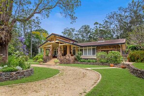 A two-story house with a stone facade, a covered porch, and a landscaped garden with a curved driveway.