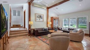 A spacious living room with a large sofa, a coffee table, and a fireplace. There is a staircase leading to an upper level, and a large window with blinds. - Brookfield Country House, Pool, 7 bedrooms (Upper Brookfield)