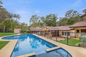 A swimming pool with a tiled deck, surrounded by a fence and a grassy area with trees.