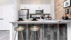 A modern kitchen with white cabinets, stainless steel appliances, and a marble countertop. There are two stools under the island. - Boutique Style Hotel -Entire Unit (Jeffersonville)