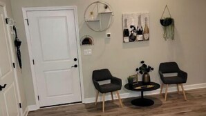 A room with a wooden floor, two black chairs, a small round table, a white door, and wall decorations including a circular mirror and framed artwork. - Boutique Style Hotel -Entire Unit (Jeffersonville)
