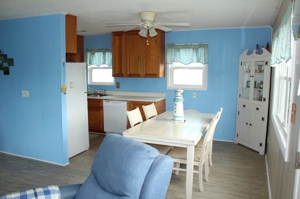 A compact kitchen with wooden cabinets, a white refrigerator, a dining table with chairs, and a ceiling fan.