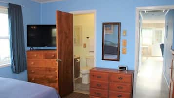 Ein Schlafzimmer mit Bett, Kommode, Fernseher und einer Tür zu einem Badezimmer.