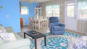 A living room with a blue armchair, a white dining table, and a patterned rug.