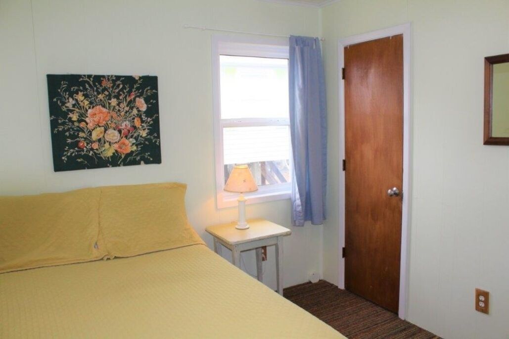 Une pièce avec un lit, une fenêtre avec des rideaux, une porte et un tableau au mur.