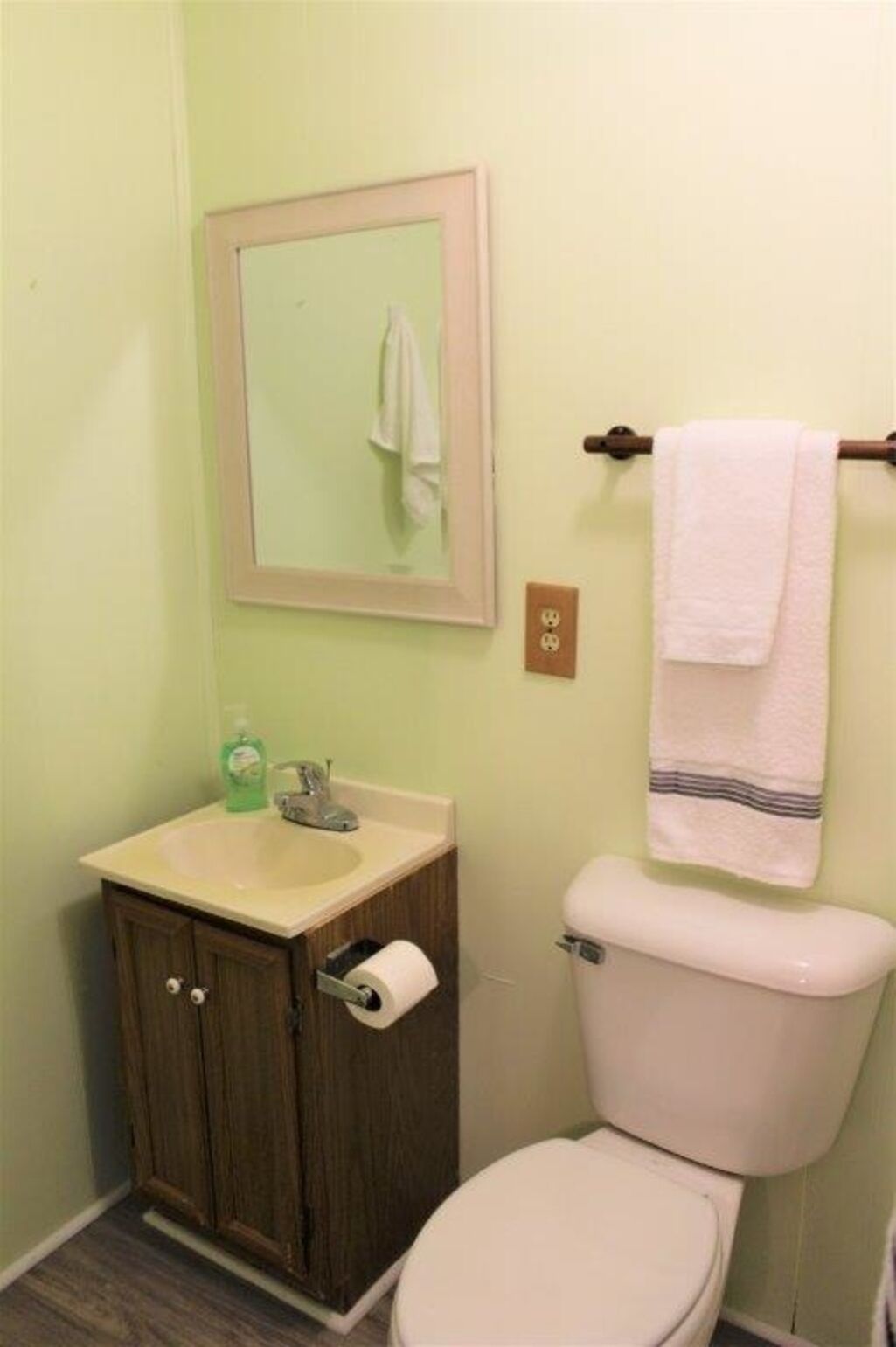 Ein Badezimmer mit Waschbecken, Spiegel, Handtuchhalter und Toilette.