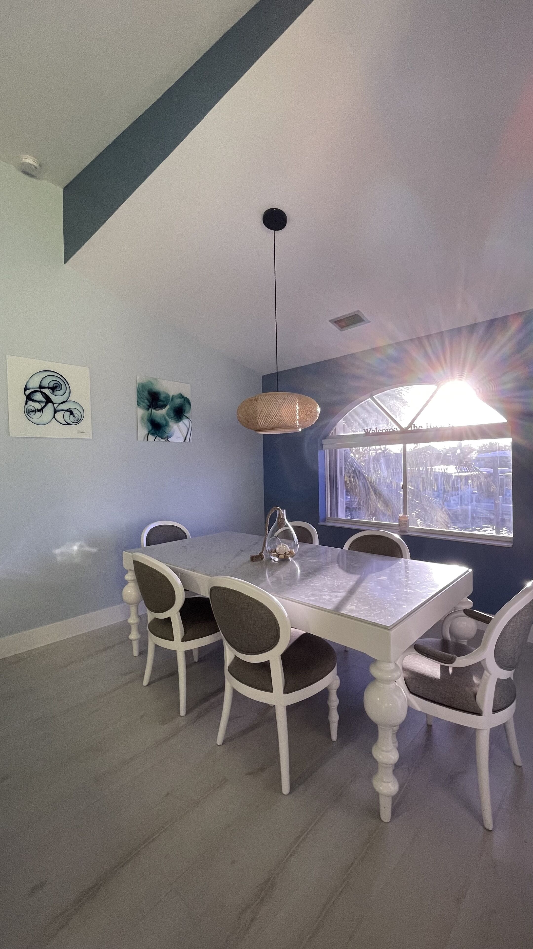 A dining area with a white table and chairs, a hanging light fixture, and artwork on the walls.