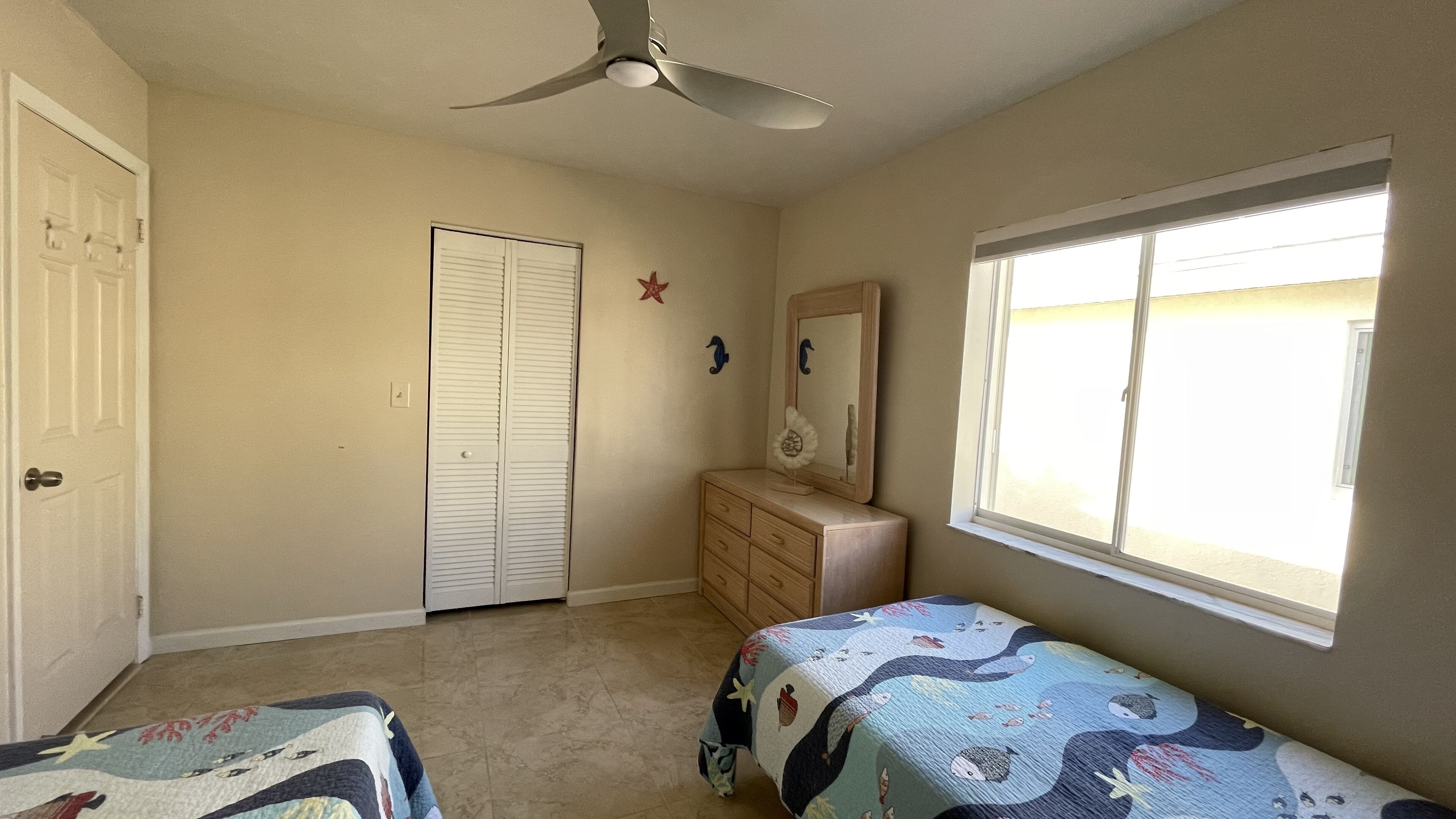 A bedroom with a bed, a dresser, a closet, a ceiling fan, and a window.
