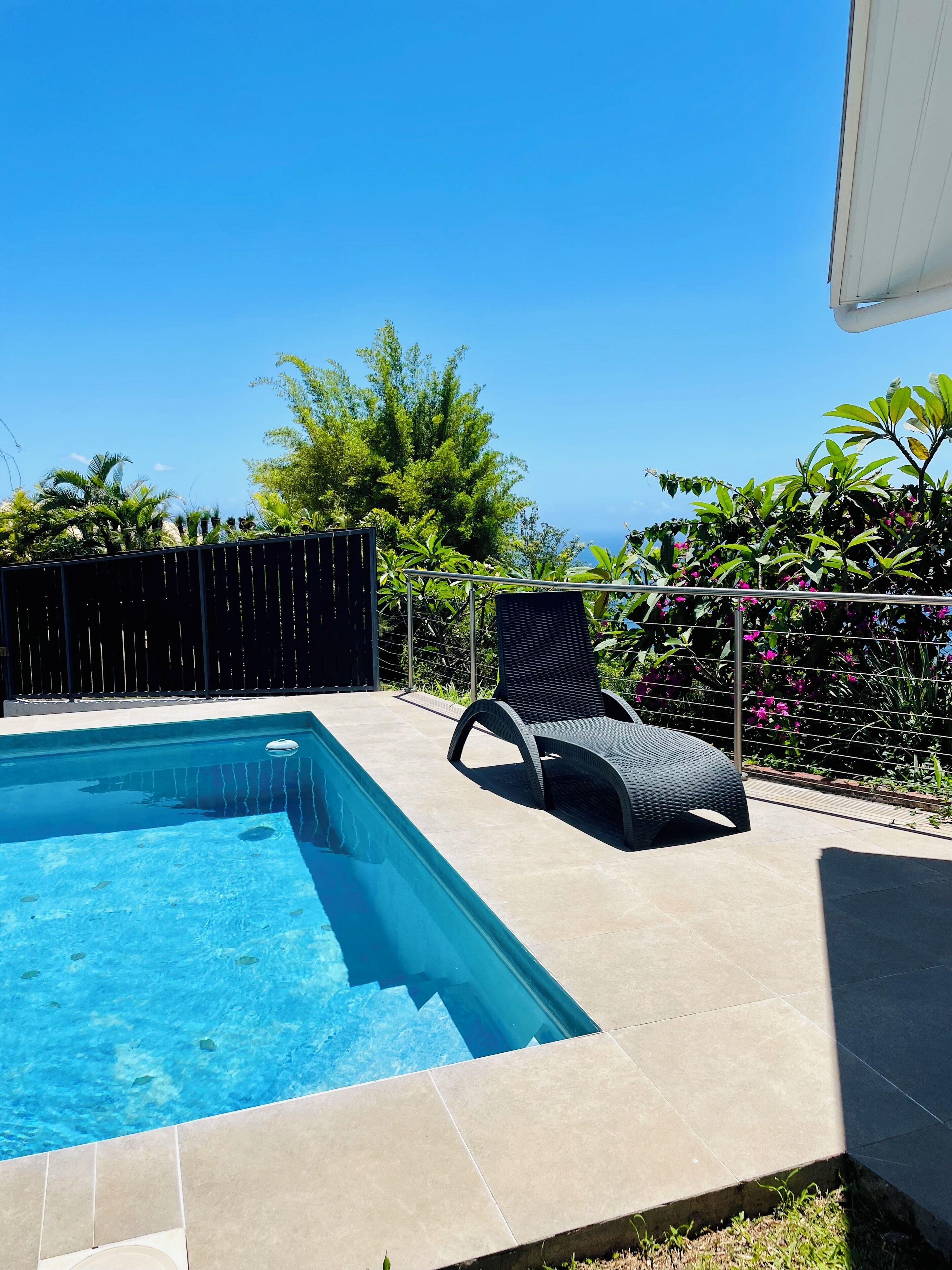 Una piscina con solárium empedrado, una silla de descanso negra y abundante vegetación de fondo.