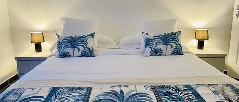 Een netjes opgemaakt bed met een bloemenprintdeken, twee bijpassende kussens en twee bedlampjes aan weerszijden.