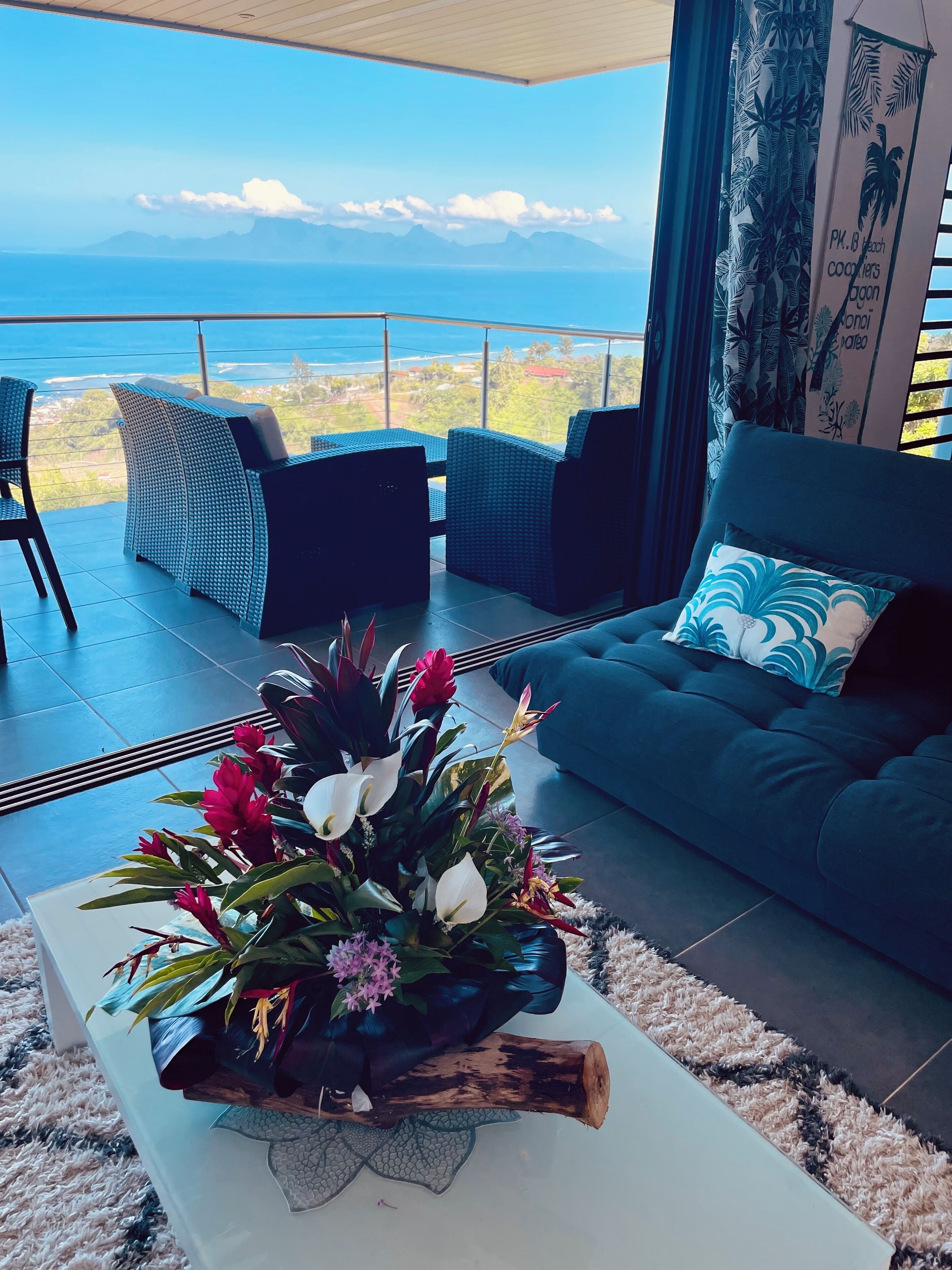 A modern living room with a view of the ocean, featuring a sofa, chairs, and a coffee table with a floral arrangement.