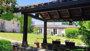 A stone building with ivy-covered walls, a covered patio, and a well-maintained garden. - Logis de caractère large reception capacity (Bressuire)