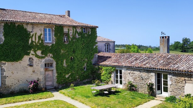 A stone building with ivy-covered walls, a tiled roof, and a small garden with a table and chairs. - Logis de caractère large reception capacity (Bressuire)