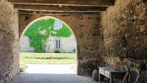 An arched doorway leading to a courtyard with a stone wall, a wooden bench, and a rustic interior. - Logis de caractère large reception capacity (Bressuire)