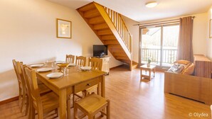 Amplia sala de estar con una mesa de comedor de madera dispuesta para cuatro personas, un sofá, una escalera y un televisor sobre un mueble.