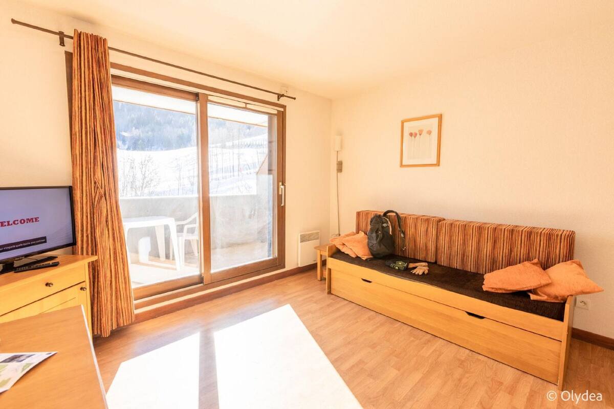 Una habitación con sofá de madera, televisor, puerta corrediza de vidrio y un cuadro en la pared.