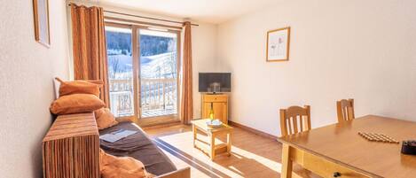 A cozy room with a sofa, a wooden dining table, and a TV.