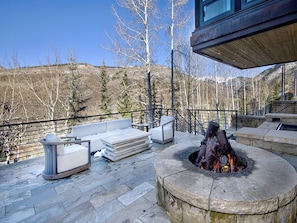 Una terraza de piedra con mobiliario exterior, un hogar y vistas a un paisaje montañoso.