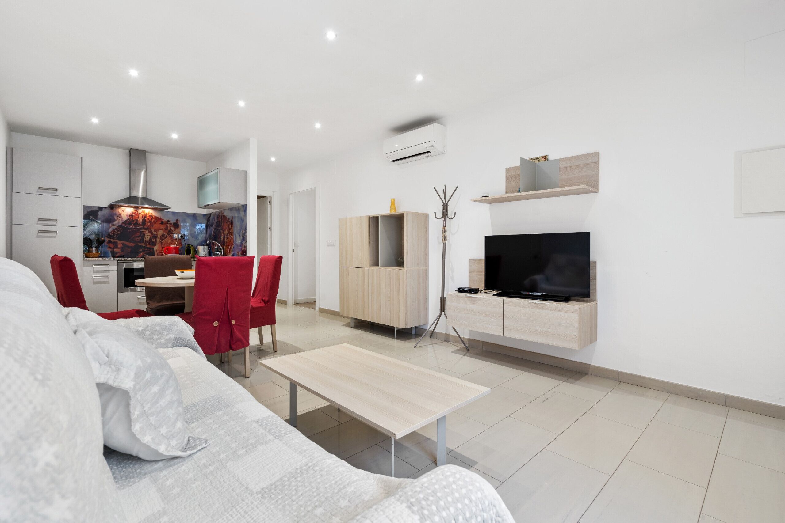 A modern living room with a sofa, a dining table, and a TV mounted on the wall.