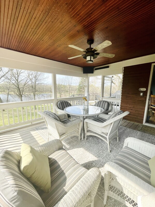 Eine überdachte Terrasse mit Korbmöbeln, einem Deckenventilator und Blick auf einen See.