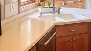Una cocina con armarios de madera, encimera blanca, un fregadero y una ventana con vistas a árboles.
