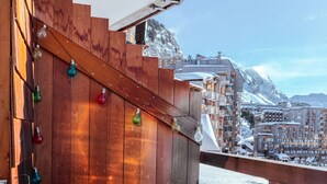 Ein Holzbalkon mit einer mit Fell bezogenen Bank, bunten Lichterketten und Blick auf einen verschneiten Berg.