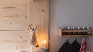 Ein hölzernes Regal mit einer dekorativen Hirschfigur und einer beleuchteten Glühbirne, ein Küchenutensilienhalter aus Holz und ein Handtuch, das an Haken hängt.