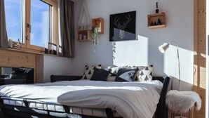Ein Schlafzimmer mit Bett, Fenster, einer Wandlampe und einem Hirschbild in einem Rahmen.