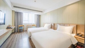 A hotel room with two beds, a desk with a chair, a TV, and a window with curtains.