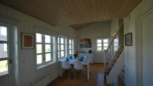 A dining area with a wooden table and chairs, a staircase, and large windows. - Panoramic Ocean & Glacier Views | Northern Lights Cottage | Hellnar, Iceland (Hellnar)