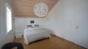 A bedroom with a wooden ceiling, a bed with a striped bedspread, a white wall with a picture, and a white door. - Panoramic Ocean & Glacier Views | Northern Lights Cottage | Hellnar, Iceland (Hellnar)