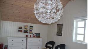 A room with a white dresser, two black chairs, a wooden ceiling, and a white wall with bookshelves and artwork. - Panoramic Ocean & Glacier Views | Northern Lights Cottage | Hellnar, Iceland (Hellnar)