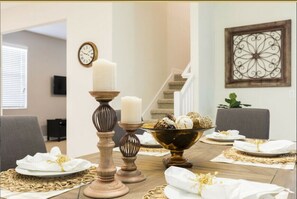 A dining area with a table set for a meal, featuring a staircase and a television in the background.