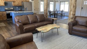 Un vaste espace de vie comprenant un canapé en cuir marron, une table basse en bois et un coin repas avec une table et des chaises en bois.