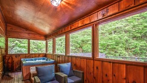 Une cabane en bois dotée d’un bain à remous, de meubles en osier et de grandes fenêtres donnant sur une forêt.