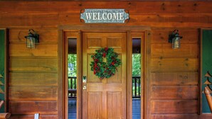 L’entrée d’un chalet en bois, ornée d’une pancarte « BIENVENUE », d’une guirlande et de deux lanternes.